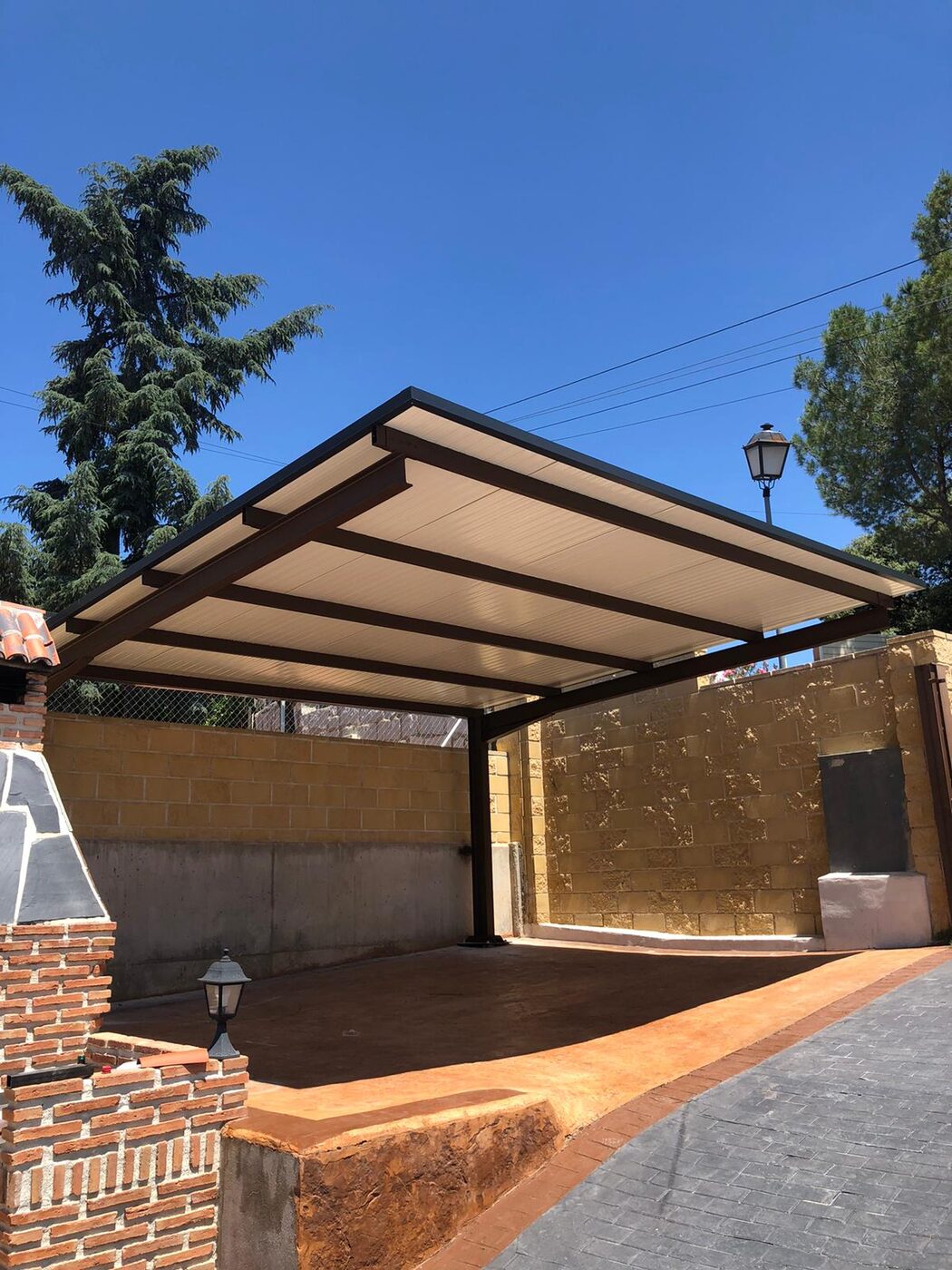 Carport en acabado oscuro tipo madera con suelo rojizo